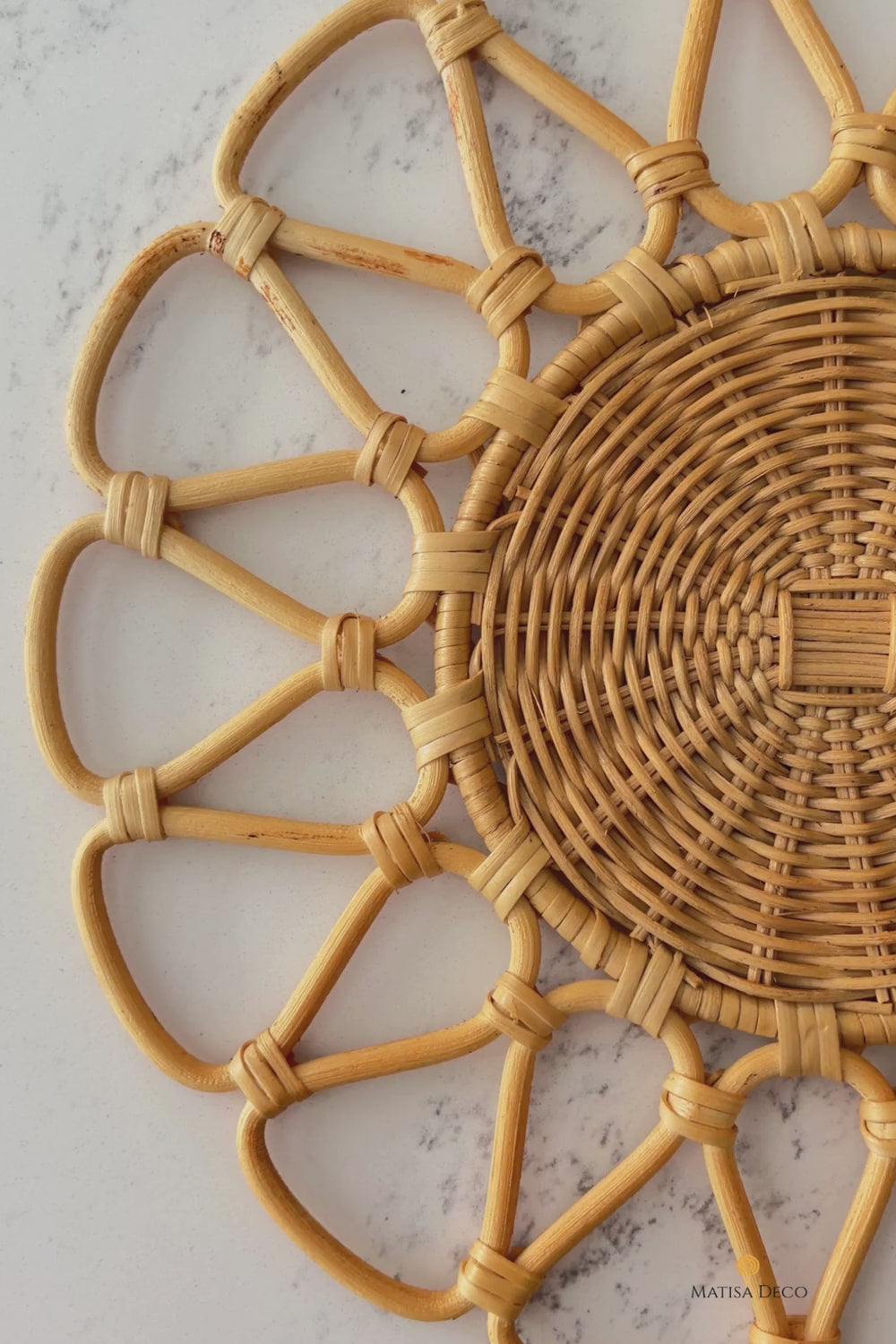 Cinematic slow-motion shot of a handwoven round natural beige rattan placemat with a sunburst floral pattern (D33cm).