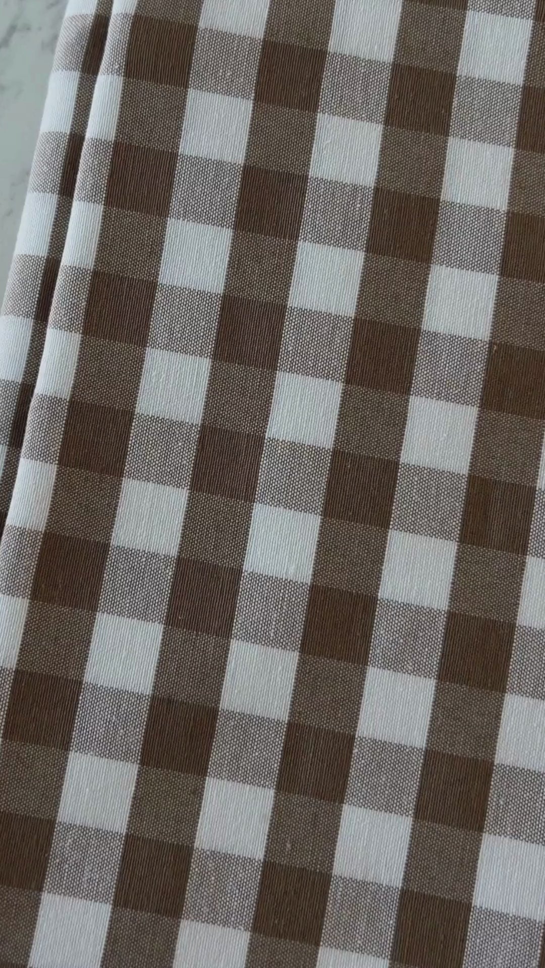 Close up video of taupe and cream gingham tablecloth highlighting its cotton rich woven texture, checked pattern and fabric finish.