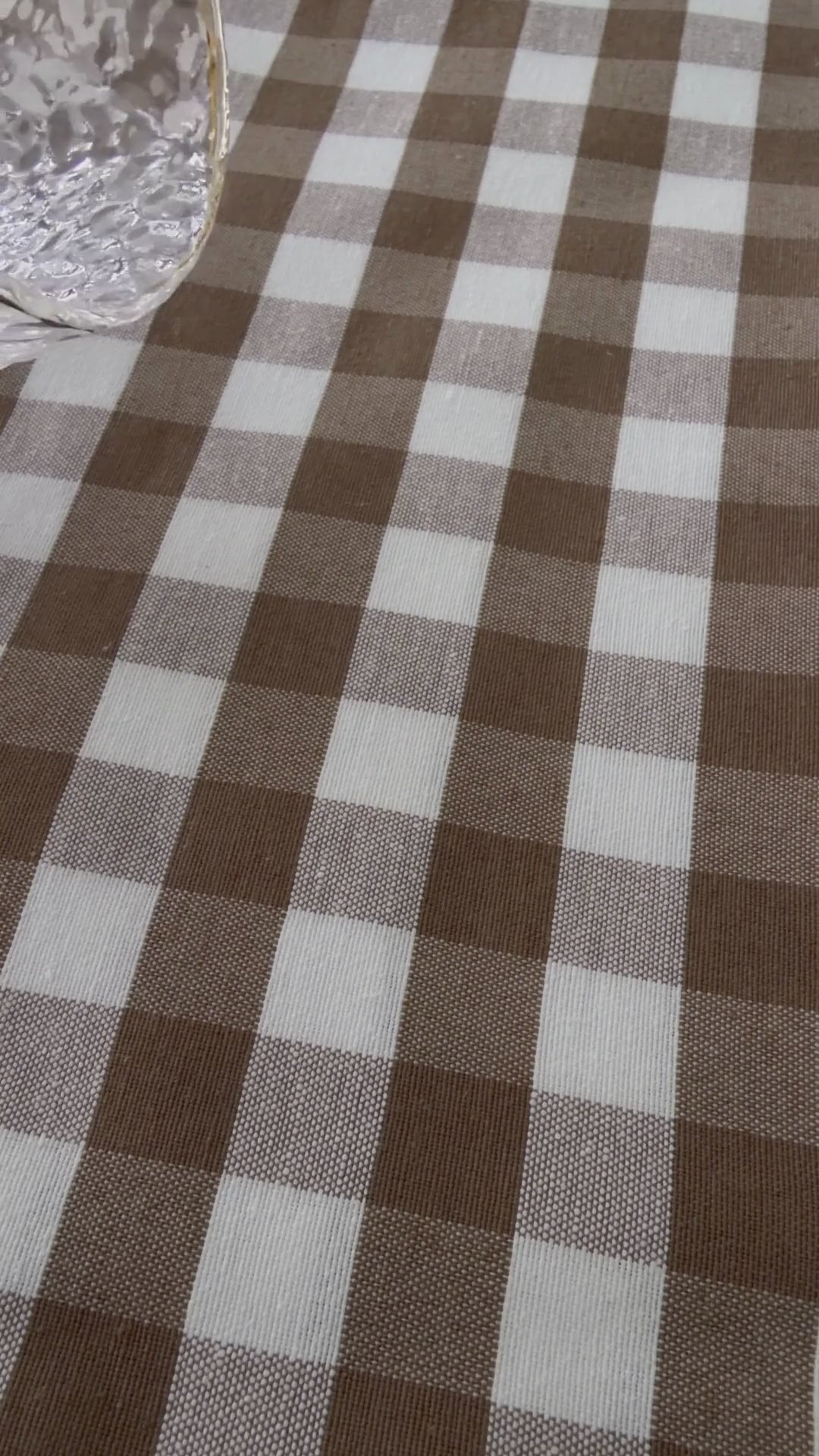 Taupe gingham water repellent tablecloth demonstration showing water beading on the fabric and being wiped away.