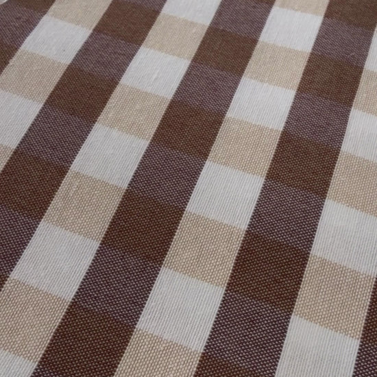 Close up demonstration of water being poured onto brown and beige gingham tablecloth fabric, forming droplets that can be wiped away.