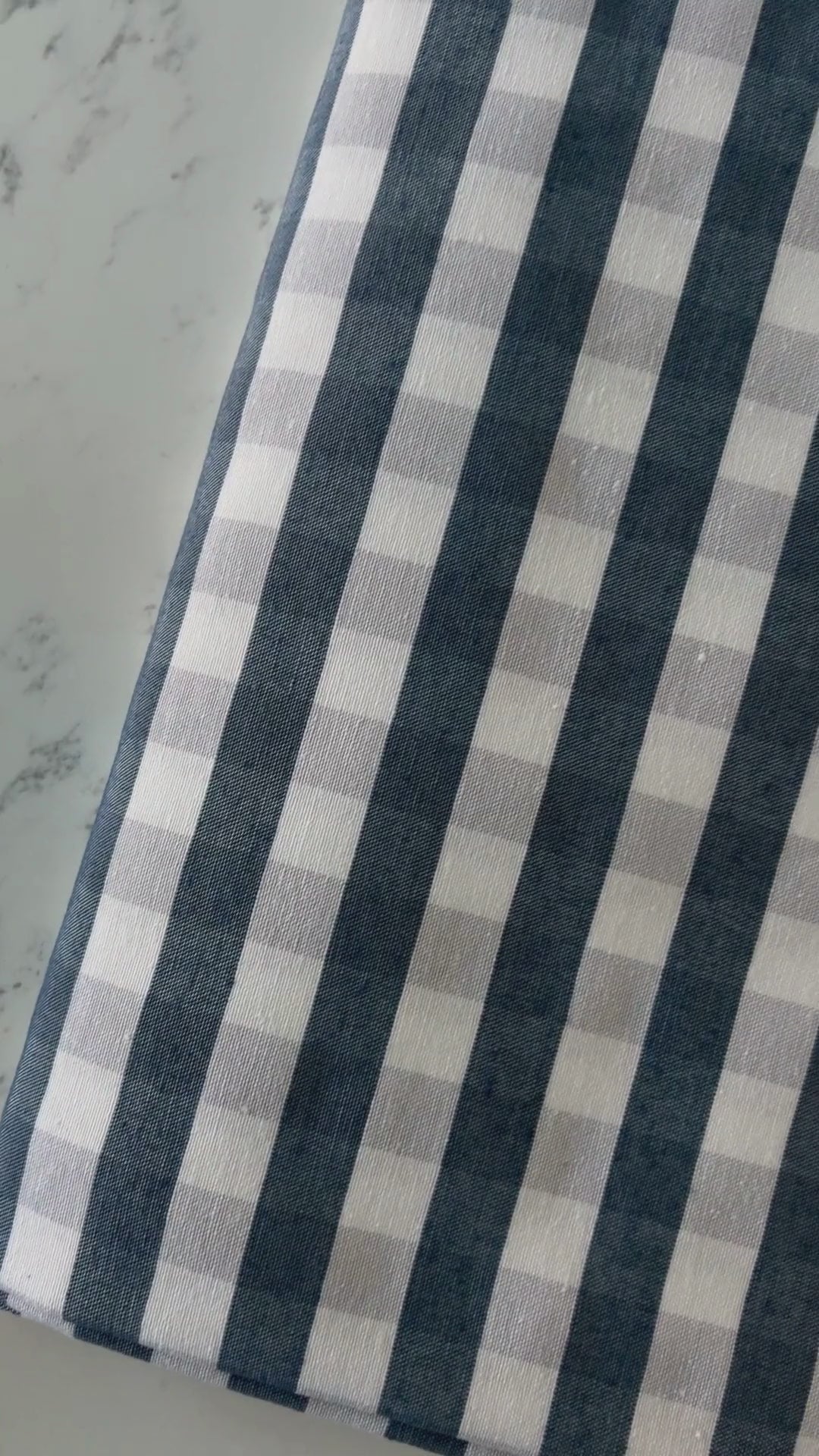 Close up video of navy blue and cream gingham tablecloth highlighting its cotton rich woven texture, checked pattern and fabric finish.