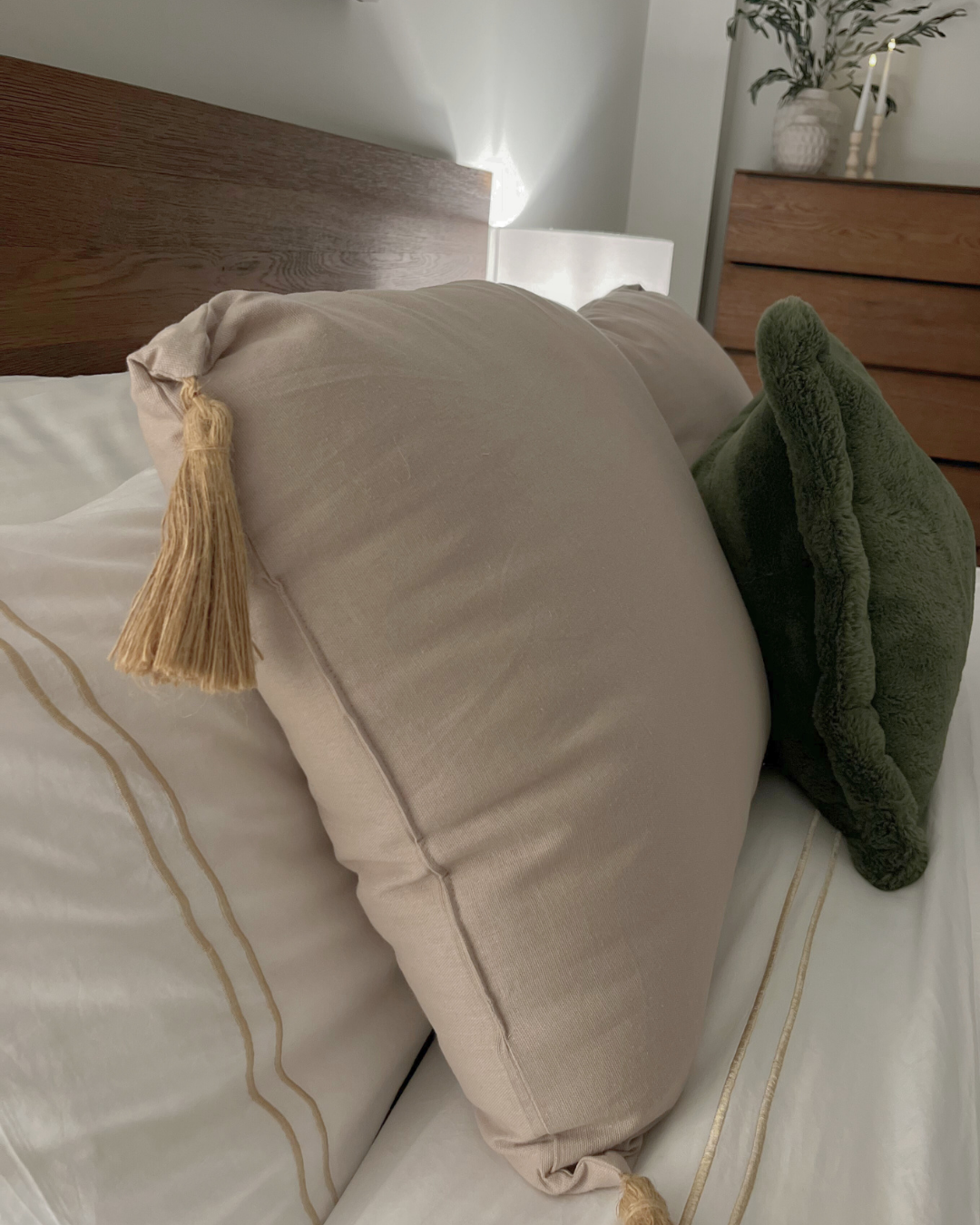 Beige pillow with tassel on a bed with a wooden headboard.