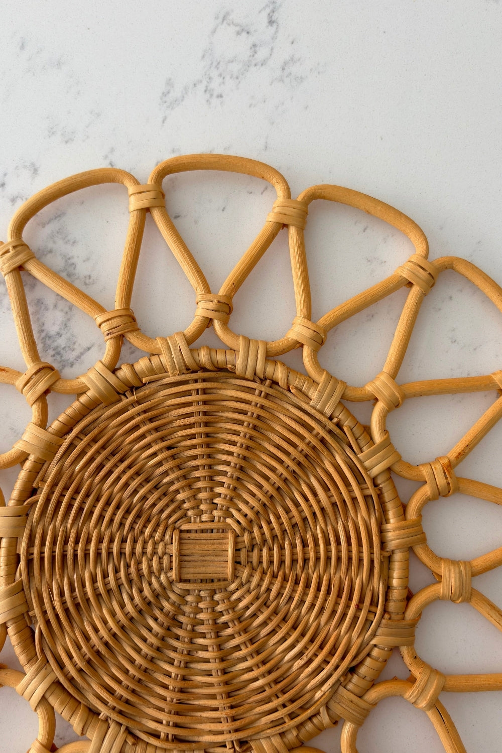 Flat lay view of the round natural beige rattan placemat laid flat on a white marble surface.