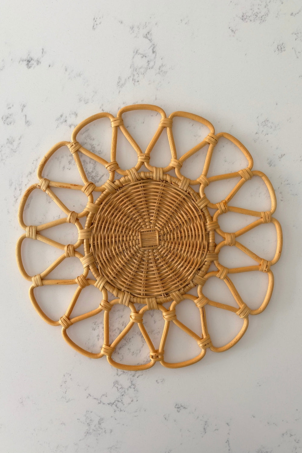 Close-up of the circular woven center and radiating looped arms on the natural beige rattan placemat by Matisa Deco.