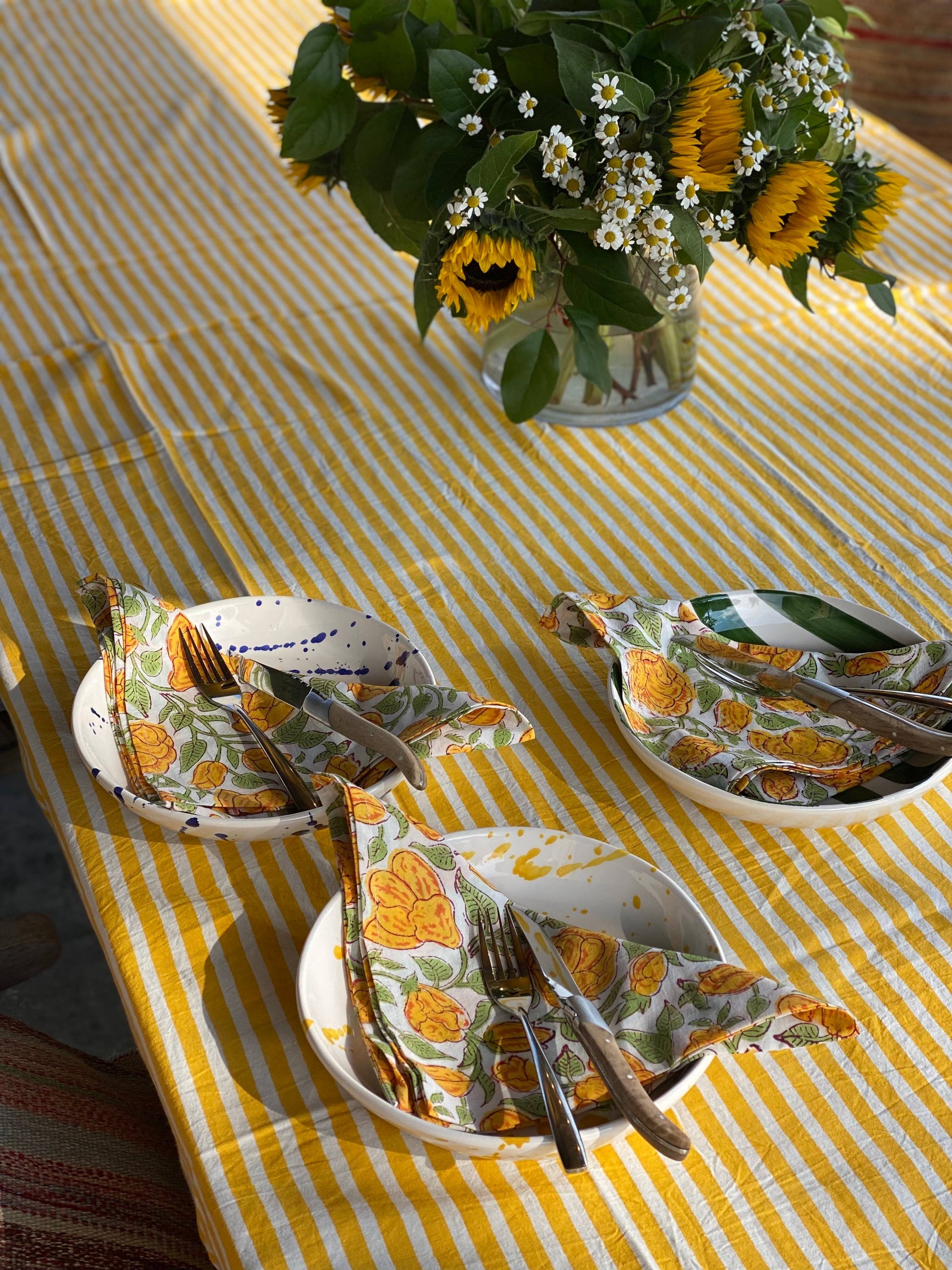 Set table with floral-patterned napkins and sunflowers on a yellow striped tablecloth