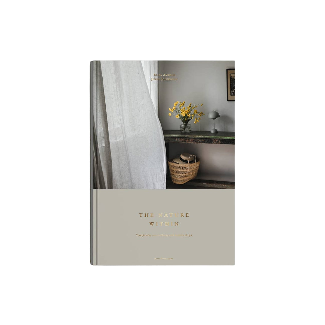 A hardcover book titled 'The Nature Within' with a beige lower cover and a cover photo showing a curtain, a console table, yellow flowers, and a woven basket, photographed on a white background.